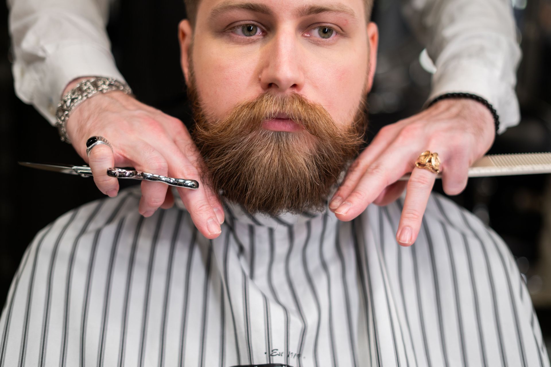 A stylish bearded man receiving precision grooming at a barbershop.